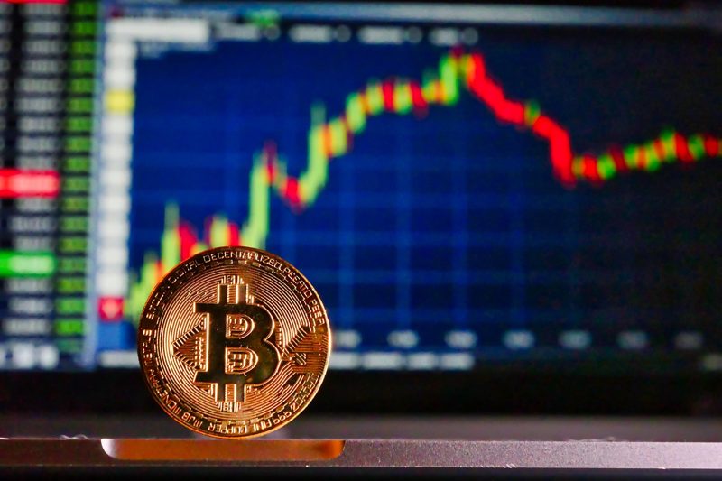 Illustration: A bitcoin on a laptop keyboard with a trading chart displayed