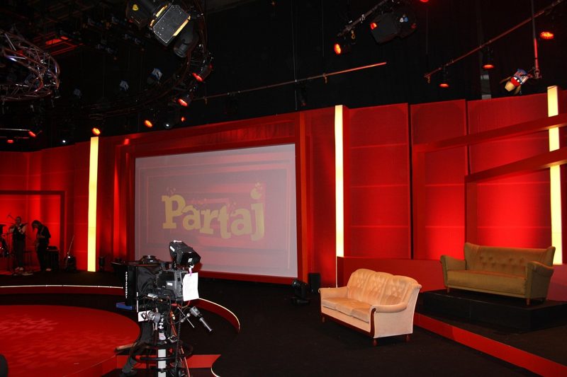Illustration: A studio stage with red panels, two sofas and cameras