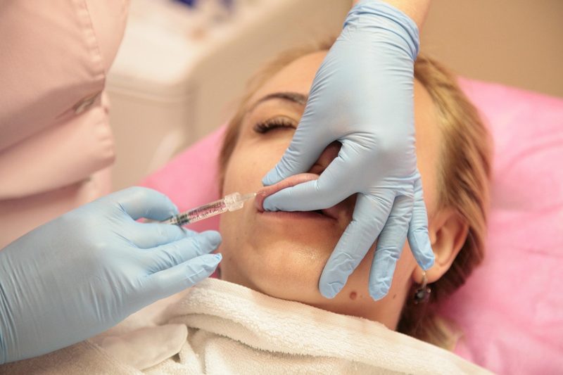 Illustration: A person receiving a lip filler injection from a gloved specialist