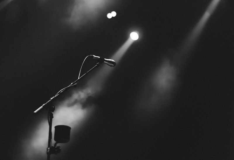 Illustration: A microphone stand on a stage illuminated by bright spotlights