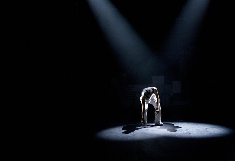 Illustration: A person in a dark shirt and white trousers under spotlights