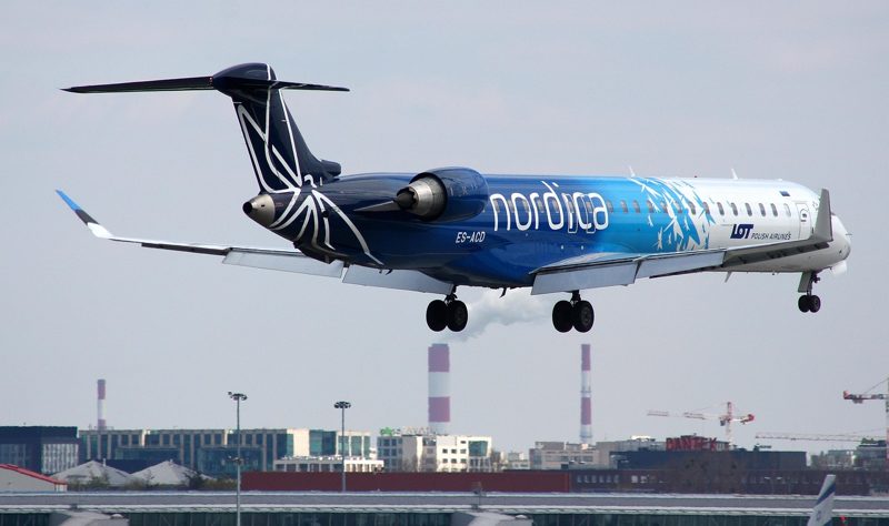 Illustration: A Nordica airliner with landing gear lowered flying over an airport