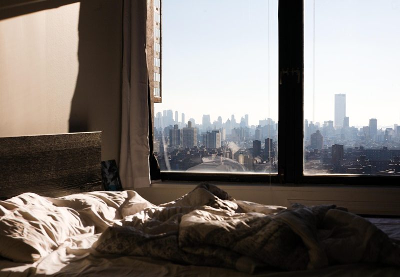 Illustration: A city skyline viewed from a bedroom with an unmade bed