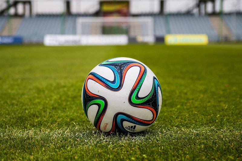 Illustration: A football on a pitch with a stadium in the background