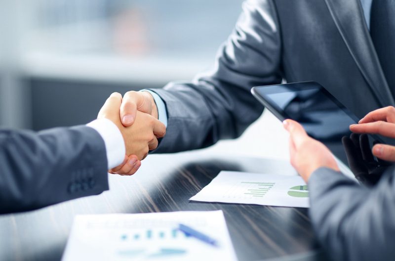 Illustration: Two business people shaking hands over a table while holding a tablet