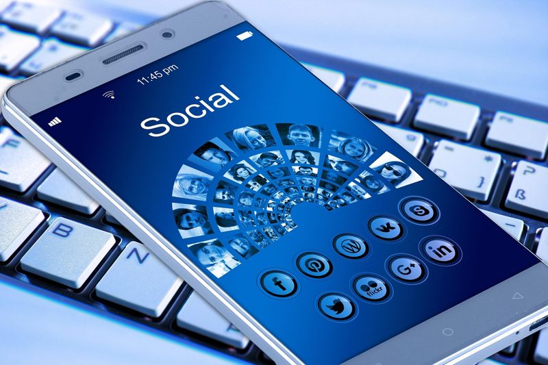 Illustration: A smartphone displaying social media icons over a keyboard