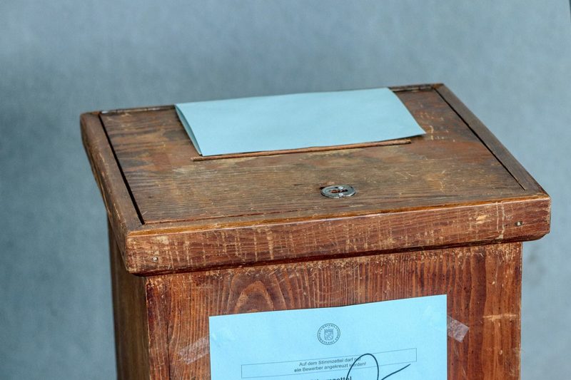 Illustration: A wooden ballot box with a blue envelope on top