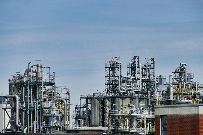 Illustration: An industrial chemical plant with metal structures and pipes against a blue sky