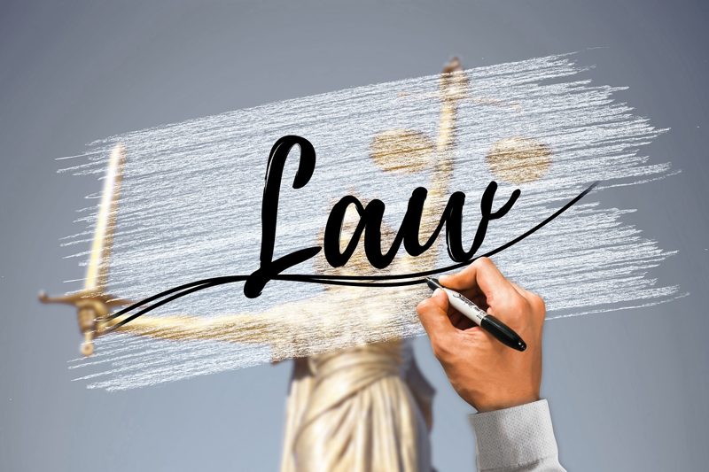 Illustration: A person writing the word law over a statue of justice