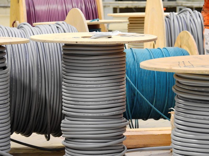 Illustration: Large wooden spools loaded with grey and blue cables outdoors