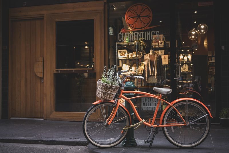 Illustration: An orange bicycle parked on the street in front of a shop