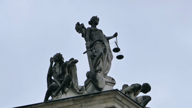 Illustration: Statues depicting justice with scales and figures against a sky