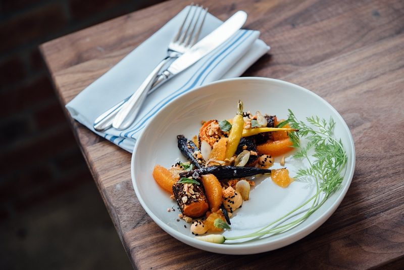 Illustration: A plate of roasted carrots with orange slices on a wooden table