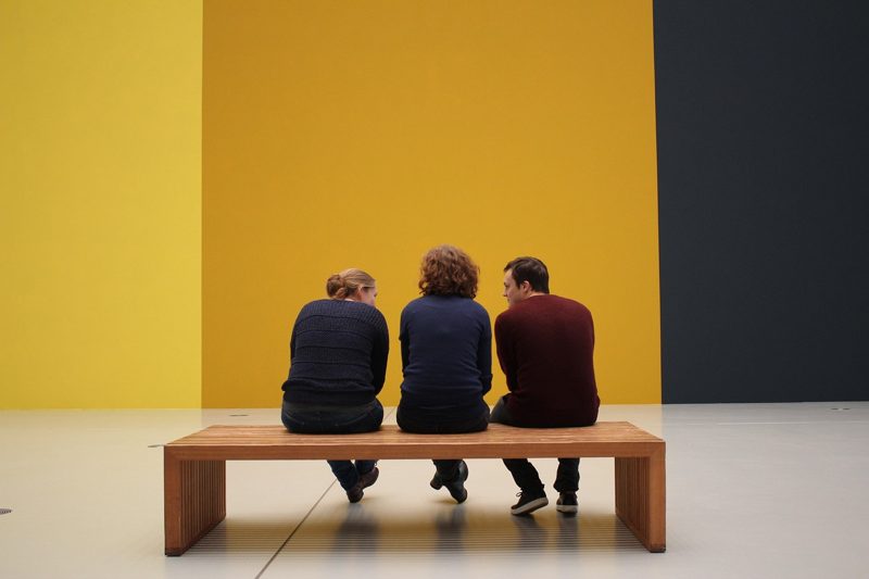Illustration: Three people sitting on a wooden bench facing a colored wall