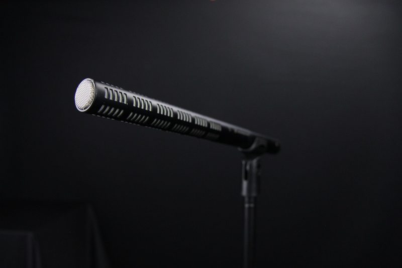 Illustration: A black shotgun microphone on a stand against a dark background