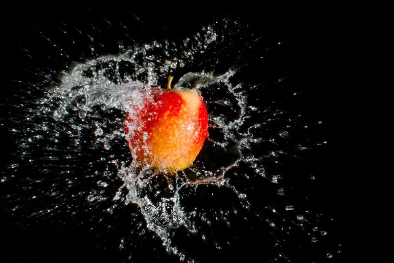 Illustration: A red apple splashing in water against a black background