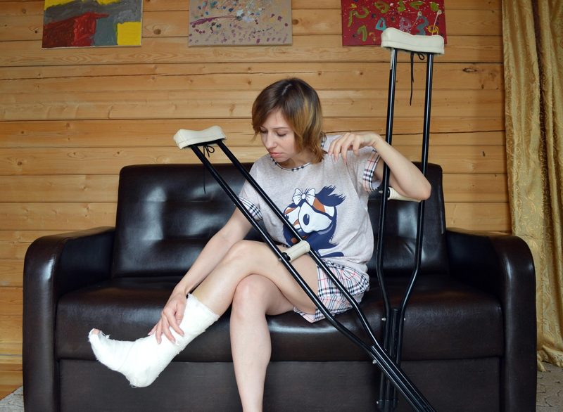 Illustration: A woman with a cast and crutches sitting on a sofa