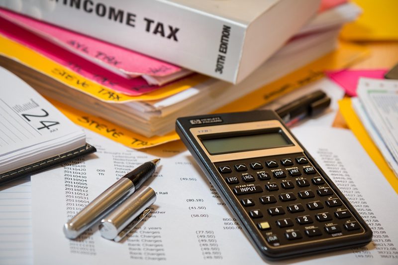 Illustration: An income tax book, papers, pens, and a calculator on a desk