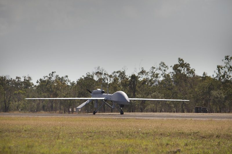 Illustration: A military drone standing on a runway with green trees behind