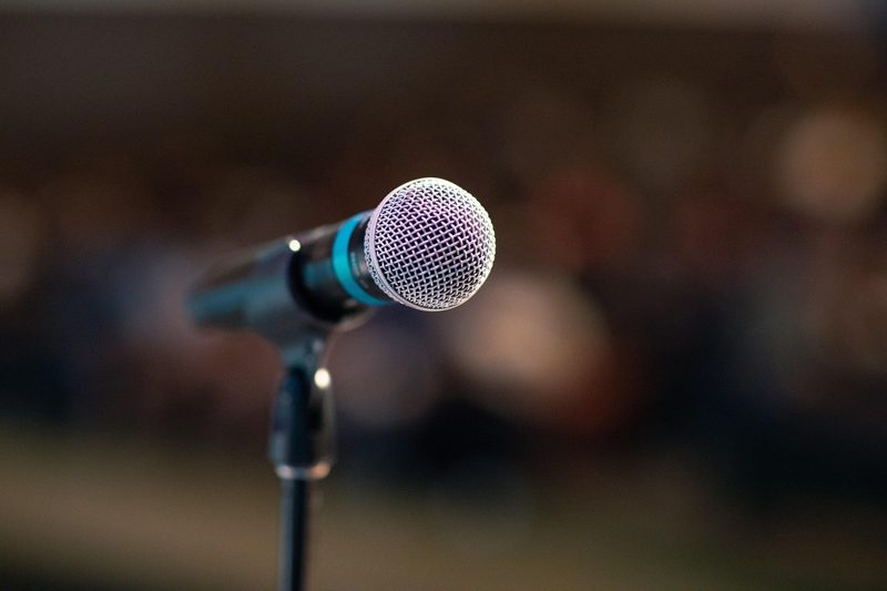 Illustration: A microphone on a stand in front of an audience