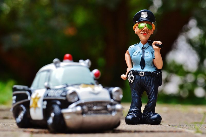 Illustration: A figurine of a police officer standing near a toy car