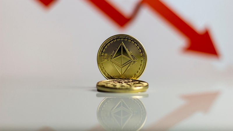 Illustration: Cryptocurrency coins against a background with a red down arrow
