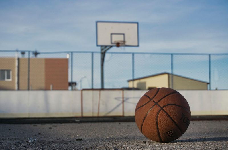 Illustration: A basketball resting on the ground with a hoop behind