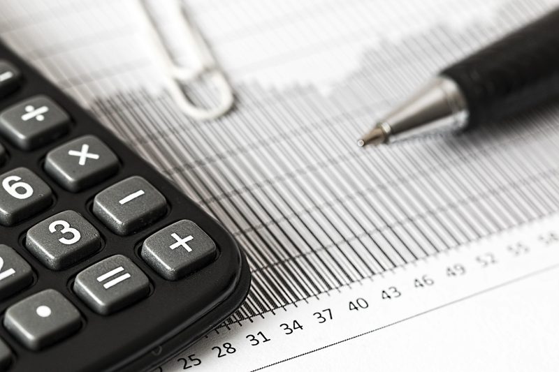 Illustration: A black calculator, pen, and paper clip on graphs