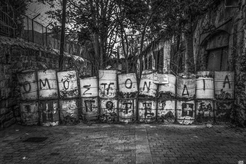 Illustration: A black and white street blocked with metal oil drums