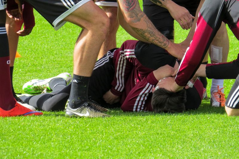Illustration: A football player lying injured on the grass surrounded by teammates