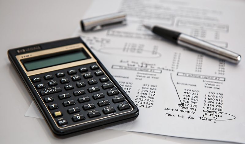 Illustration: A calculator, a pen, and financial documents rest on a table