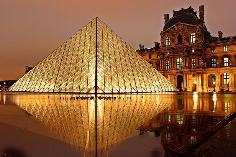 Illustration: The Louvre pyramid at night with illuminated facade and pool reflection