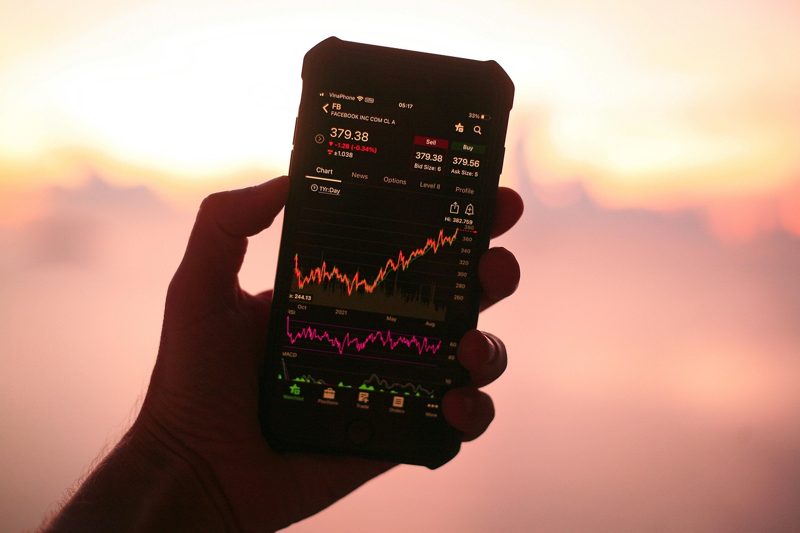 Illustration: A person holding a smartphone displaying a stock market graph