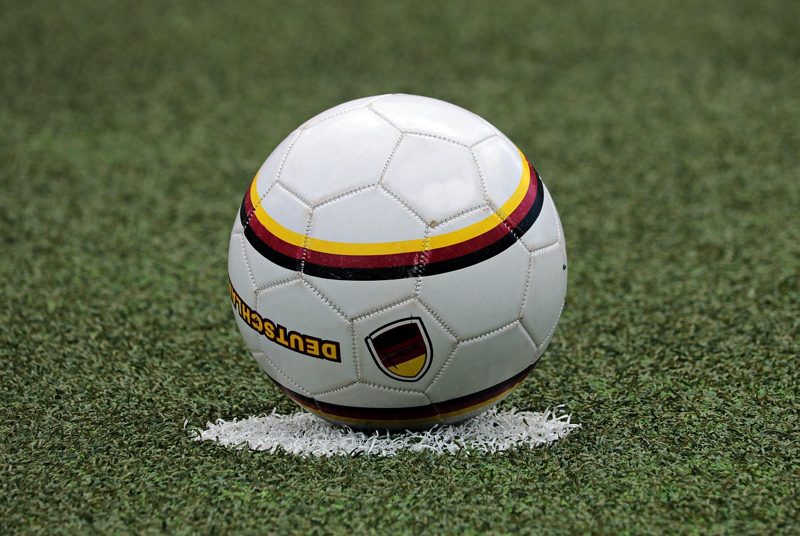 Illustration: A white football with black, red and gold details resting outdoors